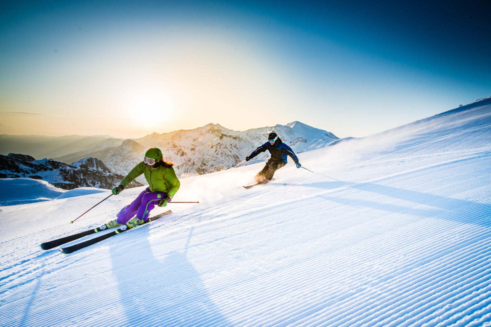 Frau und Mann beim Skifahren auf einer präparierten Piste beim Sonnenaufgang mit tollen schneebedeckten Tiroler Bergen im Hintergrund